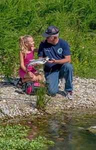Older man and young girl look at rainbow trout