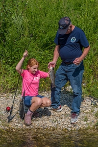 Older man with young redheaded girl and rainbow trout
