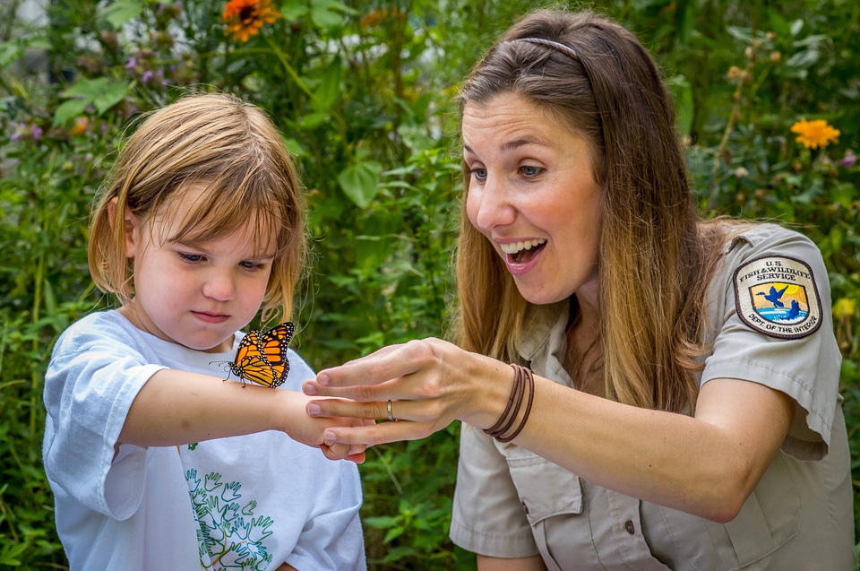 Monarch on arm of child as fws employee looks on