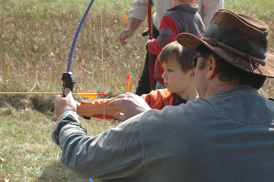 Adult teaching archery to a young boy