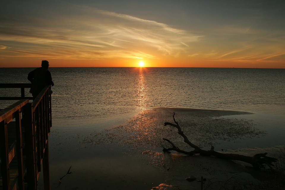 Person standing on dock looking over water at sunset