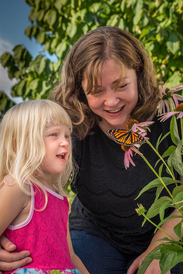 Mother and daughter view monarch on flower