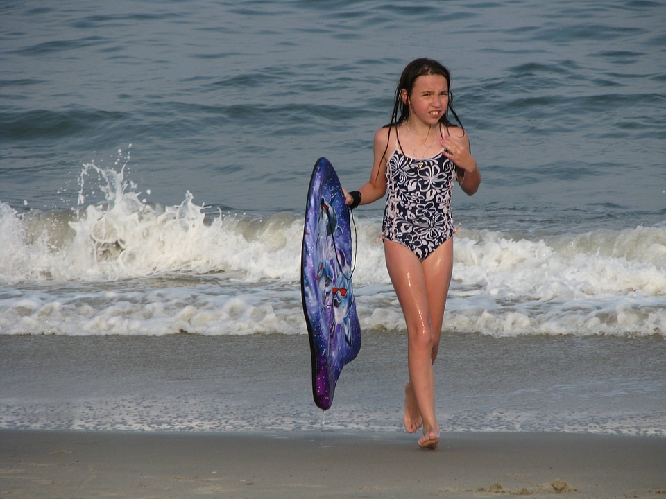 Young girl walking from the water carrying her boogie board