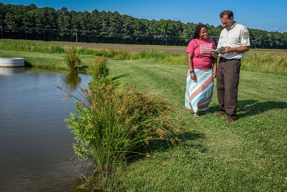 FWS Staffer shows young woman in dress a field guide by wetland