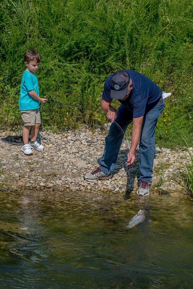 Boy fishing, older man nets rainbow trout