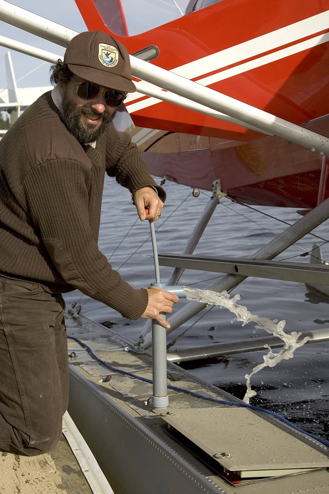 Service employee hand-pumping water by a sea plane
