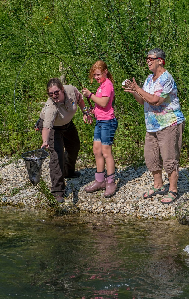 Older woman fishing with young redheaded girl, FWS employee netting trout-2