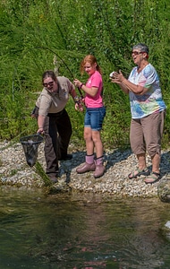 Older woman fishing with young redheaded girl, FWS employee netting trout-2