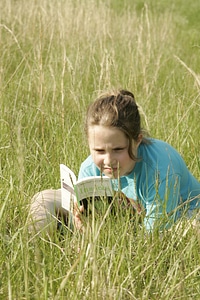 Child reading a book on a grassy field