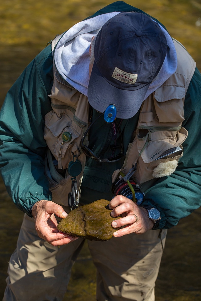 Fisherman examining rock in creek bed-3