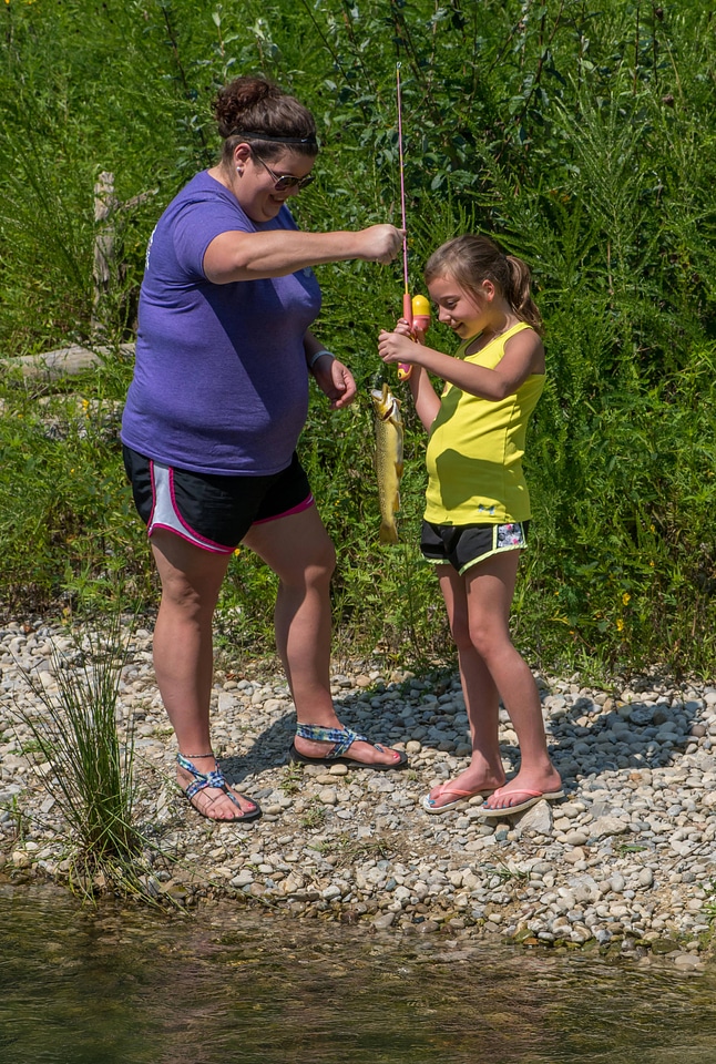 Little girl catching brown trout with mother-1