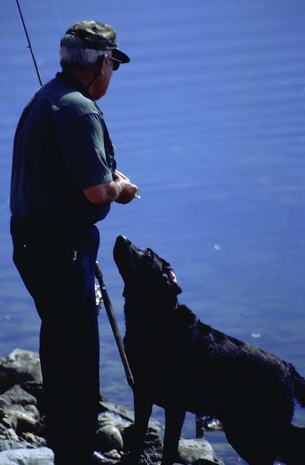 Man fishes with his dog at his side 