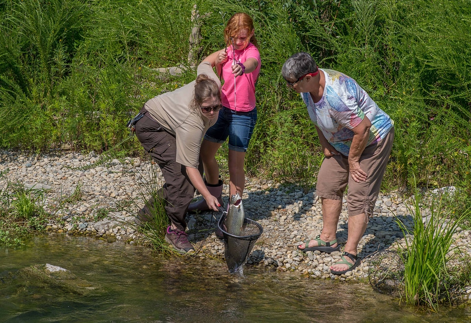 Older woman fishing with young redheaded girl, FWS employee netting trout-1