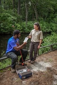 FWS hands brochure to young man sitting on rail preparing to fish