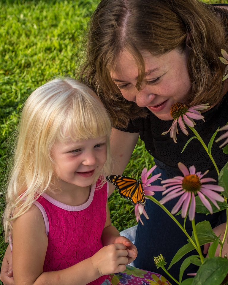 Mother and daughter look at monarch on flower-2
