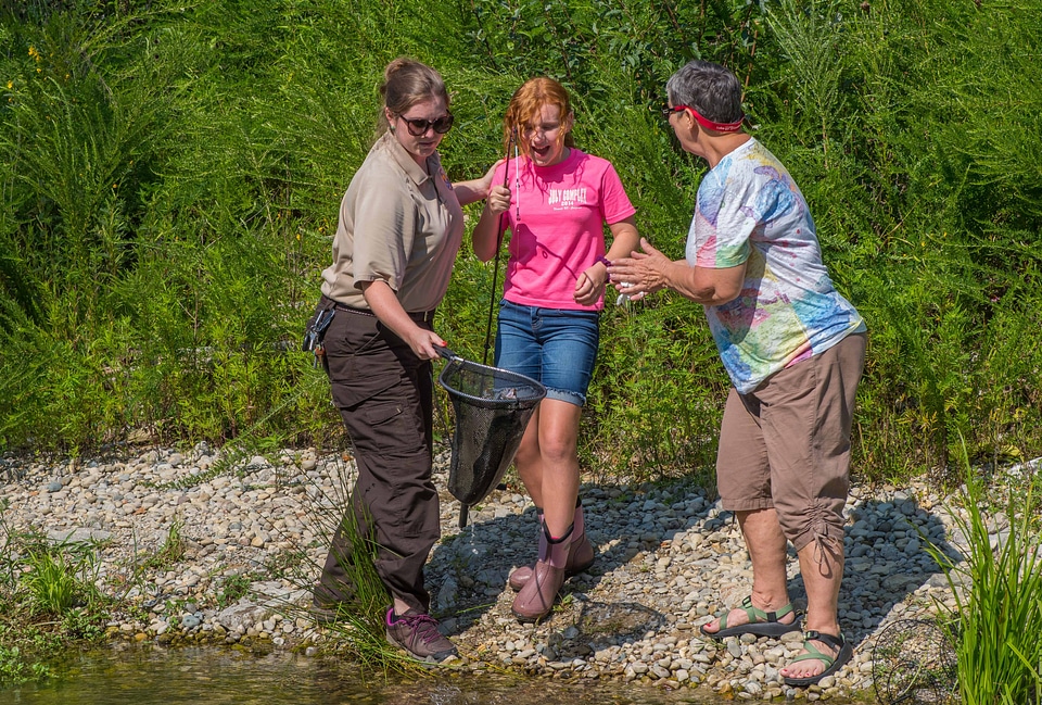 Older woman fishing with young redheaded girl, FWS employee netting trout-1