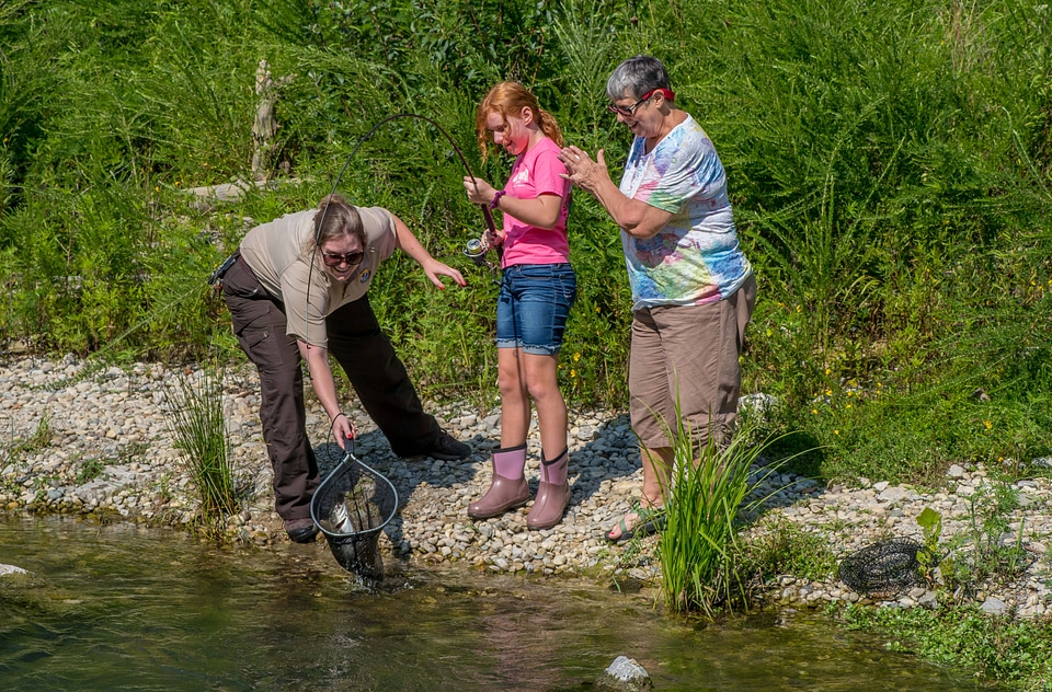 Older woman fishing with young redheaded girl, FWS employee netting trout-2