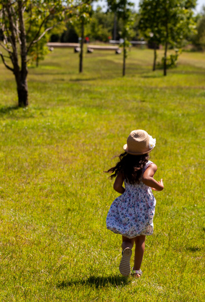 Child in hat runs on grass