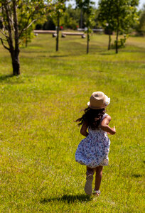 Child in hat runs on grass