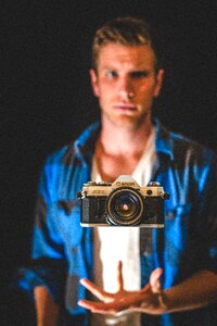 Close-up Photography of Floating Black and Gray Canon Camera in Front of Man Wearing Blue Shirt