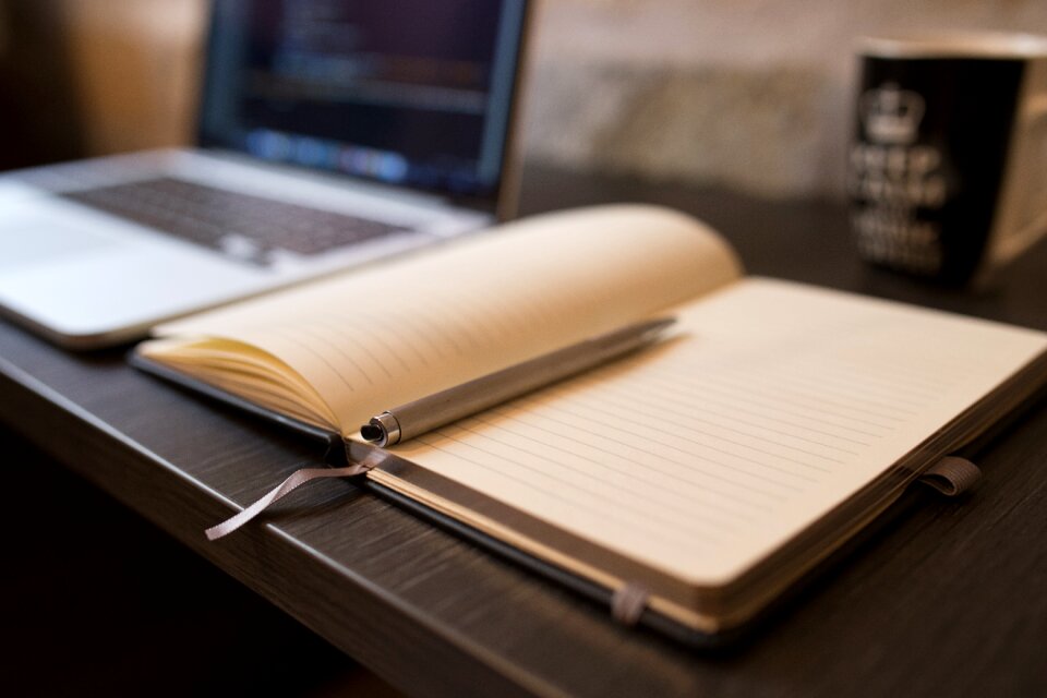 Grey Click Pen on Opened White Lined Book Beside Opened Macbook Pro on Table photo