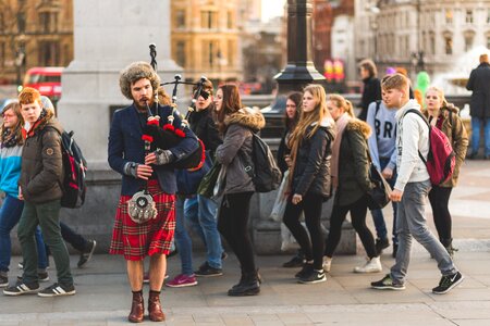 Person Using Bag Pipe Wind Instrument Near People Walking