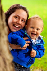 Smiling Woman Carrying Smiling Child Behind Tree Trunk photo