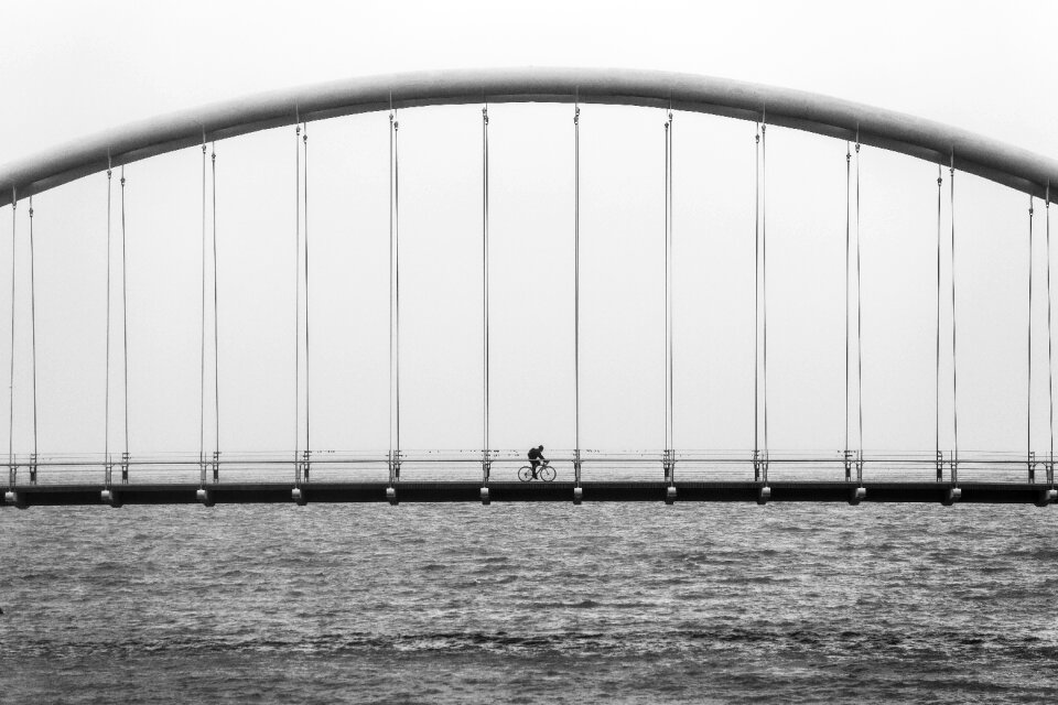 Grayscale Photography of Person Riding Bicycle on Concrete Bridge photo