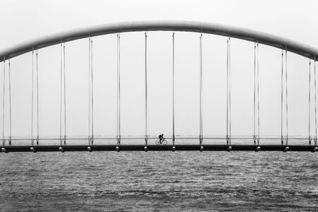 Grayscale Photography of Person Riding Bicycle on Concrete Bridge