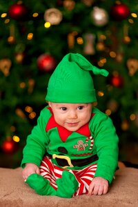 Baby Wearing Green Elf Costume Sitting on Brown Rug photo