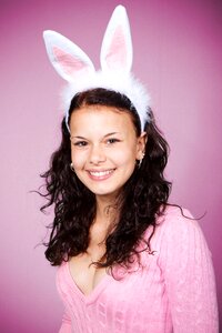 Woman in Pink Sweater Wearing Bunny Headband Smiling Against Pink Background photo