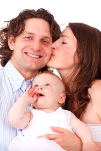 Brown Haired Woman Kissing Man in Blue White Dress Shirt Holding Baby in White Dress photo