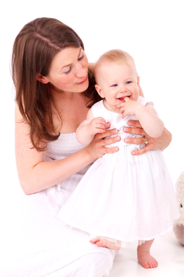 Brown Haired Woman Wearing White Strapless Dress Holding Bay Wearing White Sleeveless Dress photo