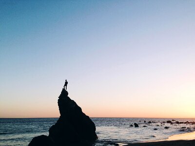 Silhouette of Person Standing on Rock on Beach Shore during Yellow Sunset photo