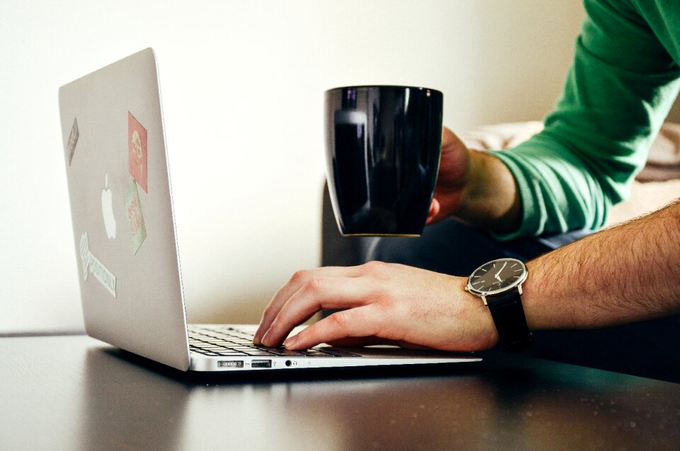 Person Wearing Green Long Sleeve Shirt Holding Black Ceramic Mug and Macbook Air
