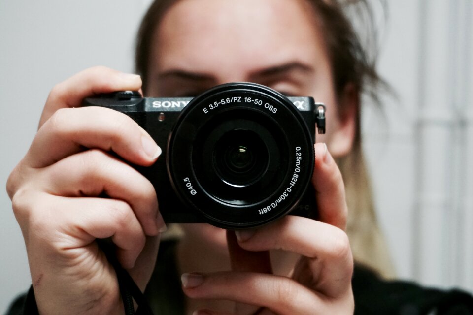 Woman Holding Black Sony Dslr Camera Taking a Photo of Herself at Mirror