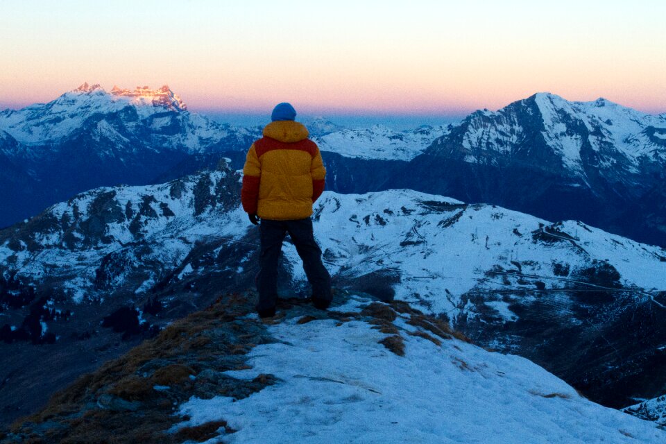 Person in Orange and Red Winter Jacket on Top of Snow Covered Mountain