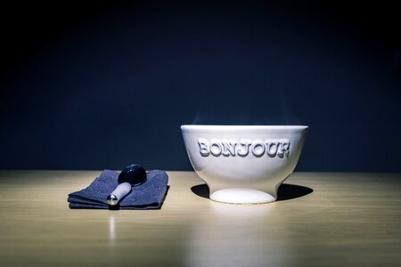 Bonjour Embossed White Ceramic Bowl on Table Beside Stainless Steel Spoon on Black Table Textile photo
