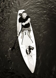 Man Standing on Surfboard on Water Rowing in Greyscale Photography photo