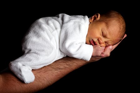 Baby in White Onesie Sleeping on Person's Hand photo