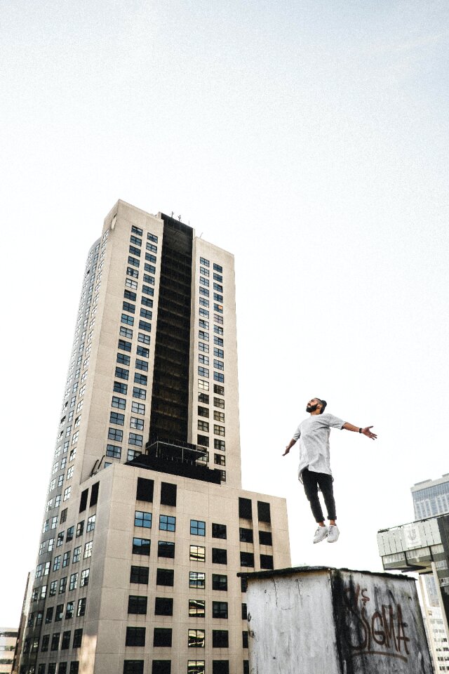 Man Wearing White Long Sleeve Shirt Beside White and Black High Rise Building