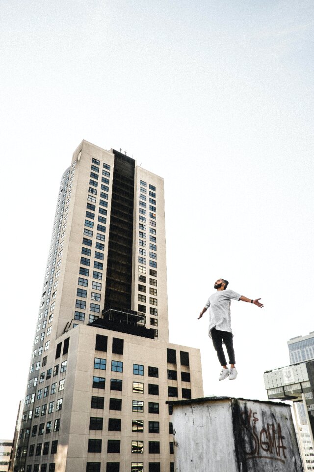 Man Wearing White Long Sleeve Shirt Beside White and Black High Rise Building photo