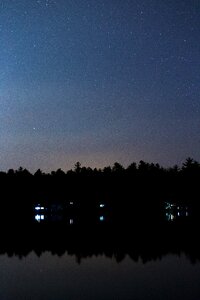 Silhouette of Trees Reflecting on Body of Water Under Starry Night Skies