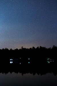 Silhouette of Trees Reflecting on Body of Water Under Starry Night Skies photo