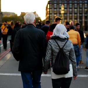Man in Black Jacket Beside Woman in Grey Leather Jacket Holding Hands at Dusk in Busy Street photo