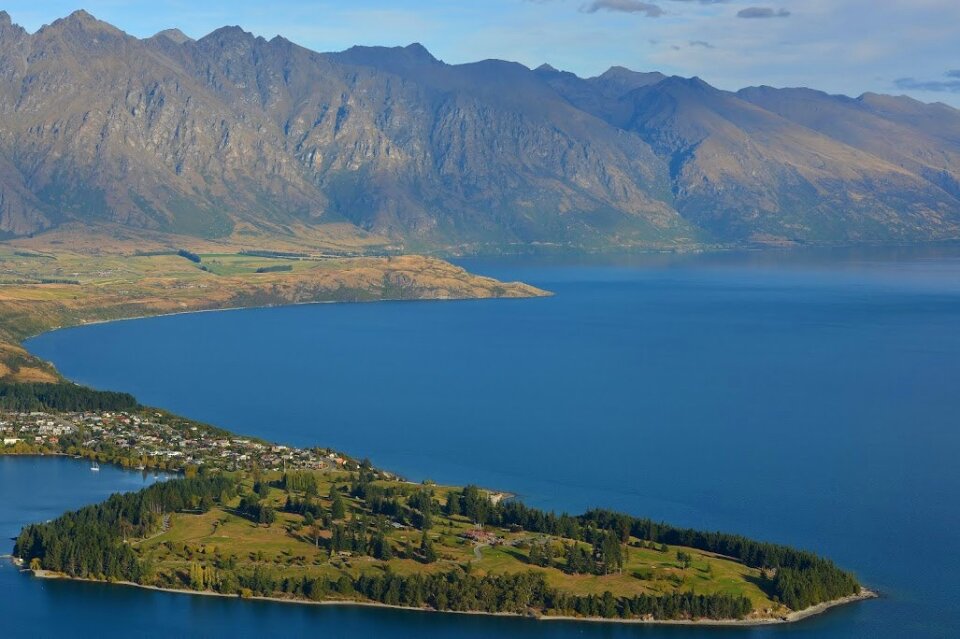 Green Field Island in the Middle of Body of Water Near Mountains during Daytime