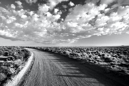 Grayscale Photo of Empty Road Between Grass Field Under Cloudy Sky photo