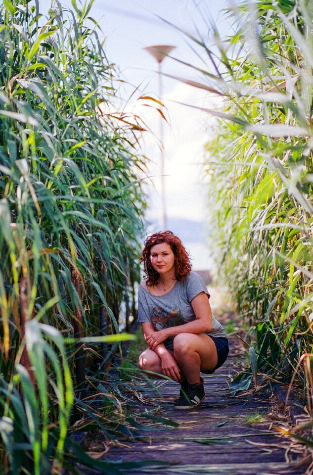 Woman in Gray and Red Scoop Neck T-shirt Seating in Between of Green Plant during Daytime