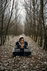 Man Wearing Gray Black Zip Hoodie Jacket Praying in Between Black Tree during Daytime photo