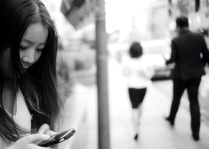 Woman Using Smartphone at Sidewalk Near Man and Woman Walking Away from Her photo